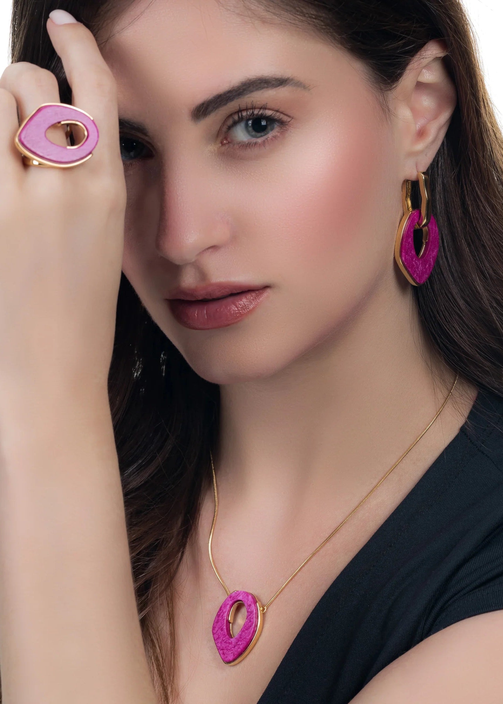 Woman wearing pink and gold jewelry including a ring, earrings, and necklace on a white background