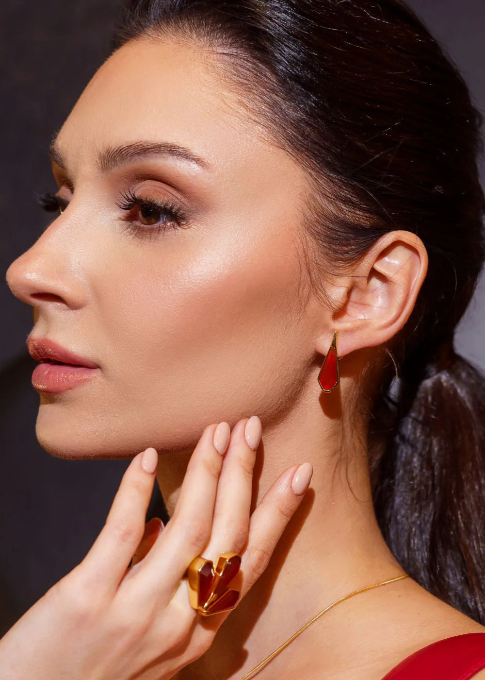 Woman wearing red earrings and ring, with a dark background