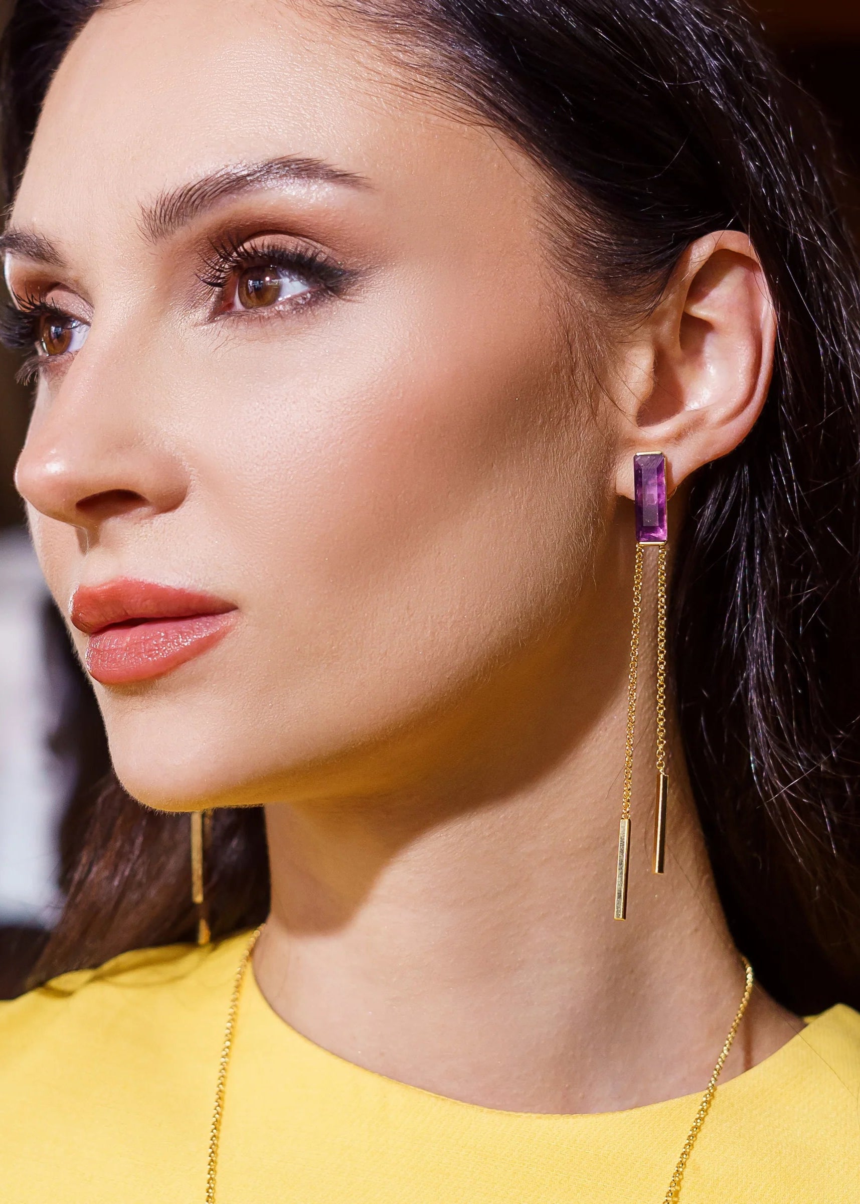 Woman wearing a gold earring with a purple gemstone on a blurred background