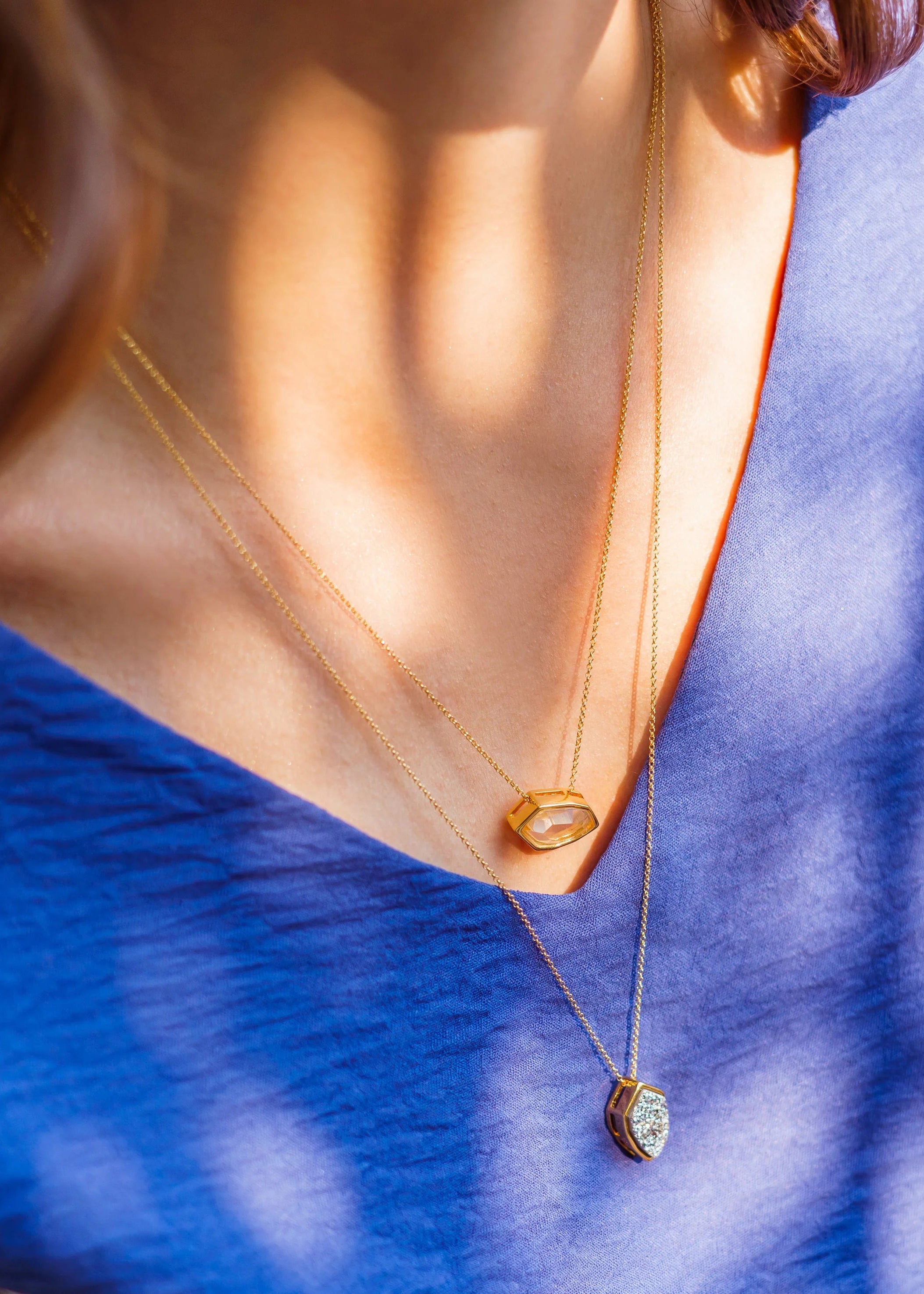 Gold necklace with a pendant worn by a person against a blue fabric background