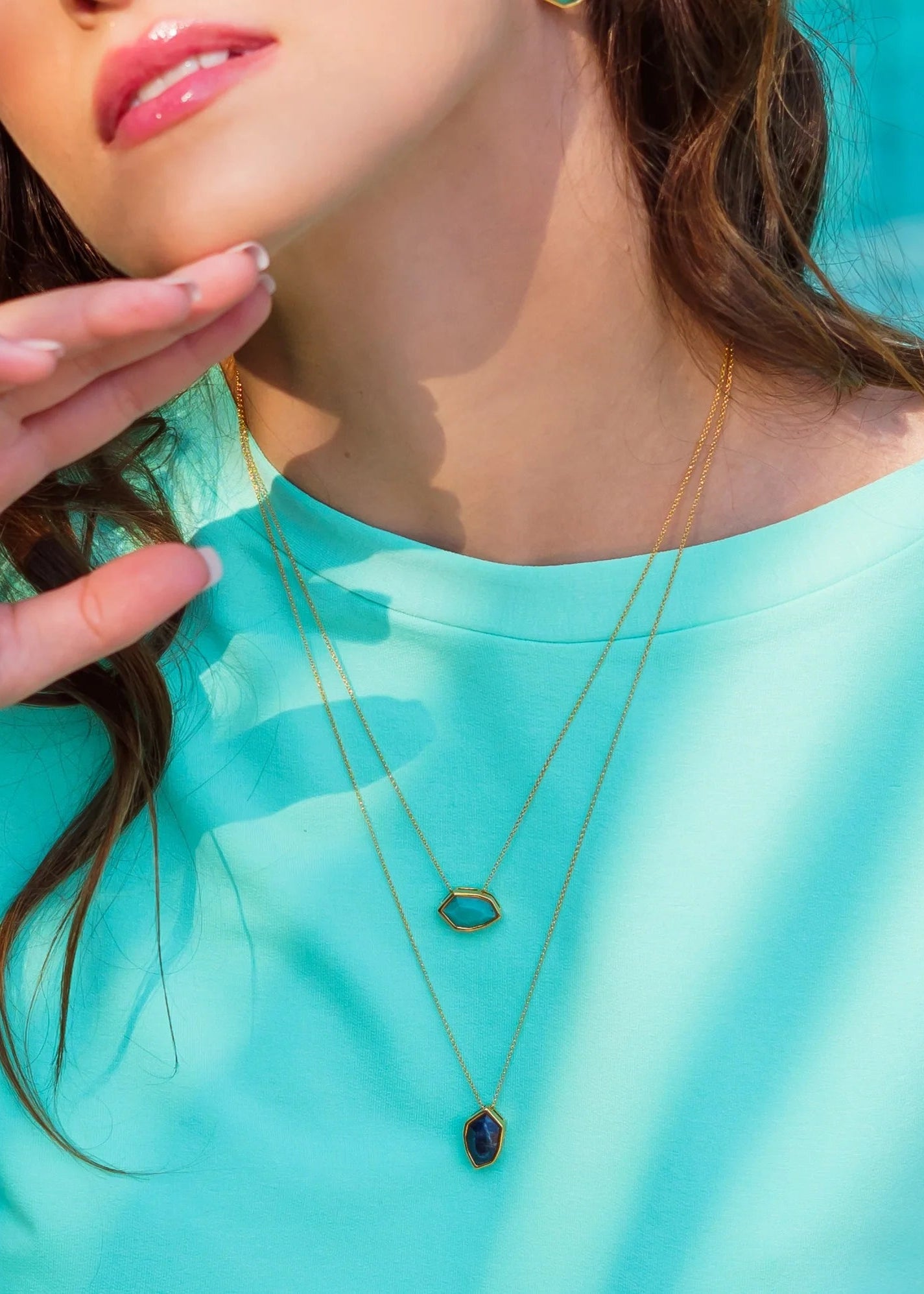 Woman wearing a turquoise top with gold necklaces against a blurred background