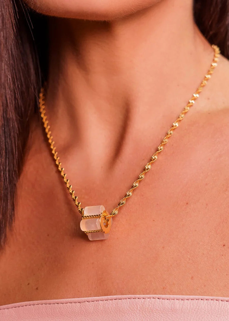 Gold necklace with a pink pendant worn by a person