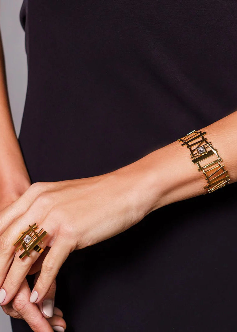 Close-up of a person's hands wearing gold rings and a bracelet on a dark background