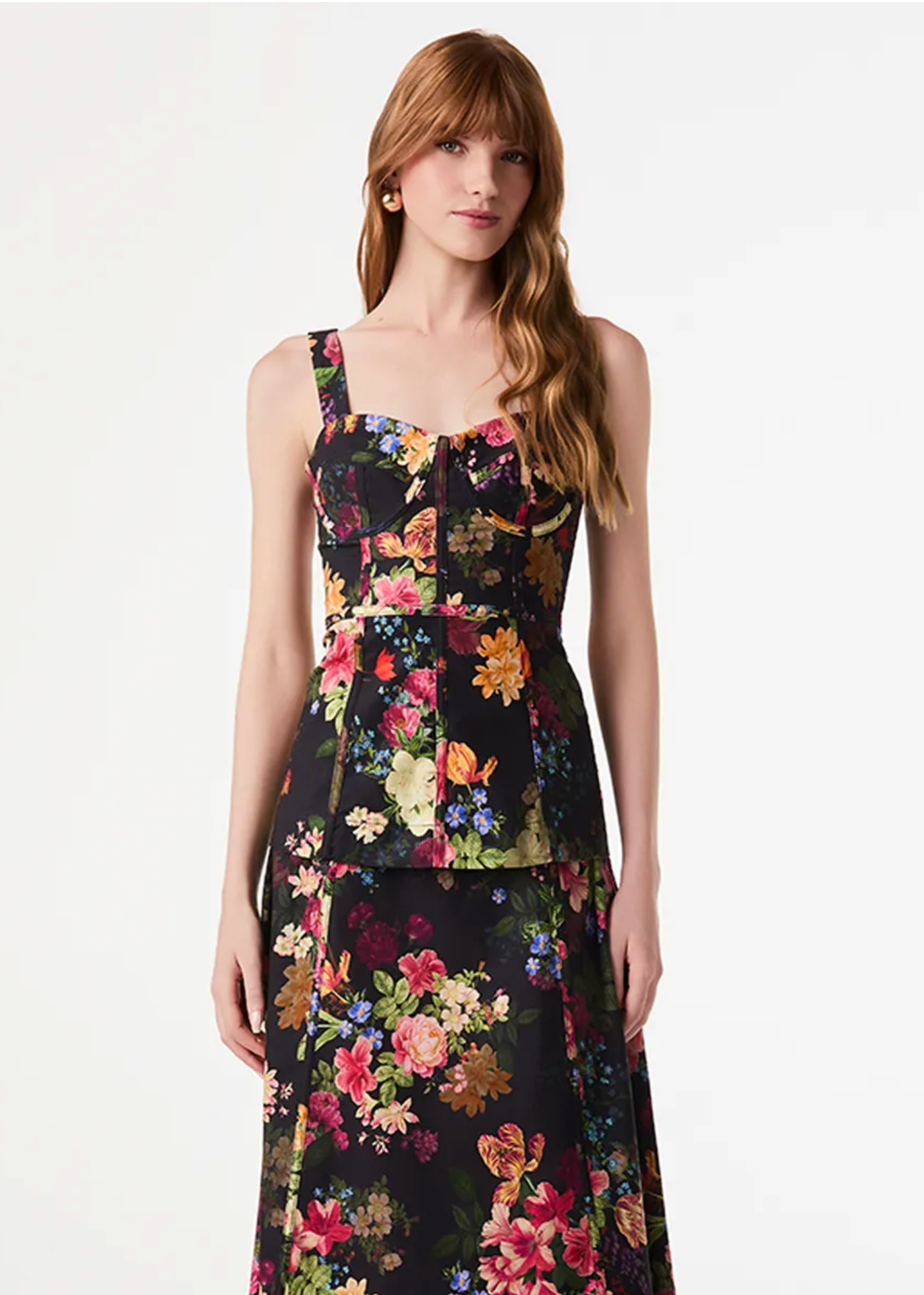 A woman modeling a sleeveless black midi dress with a vibrant multicolor floral print, photographed against a plain white studio background.