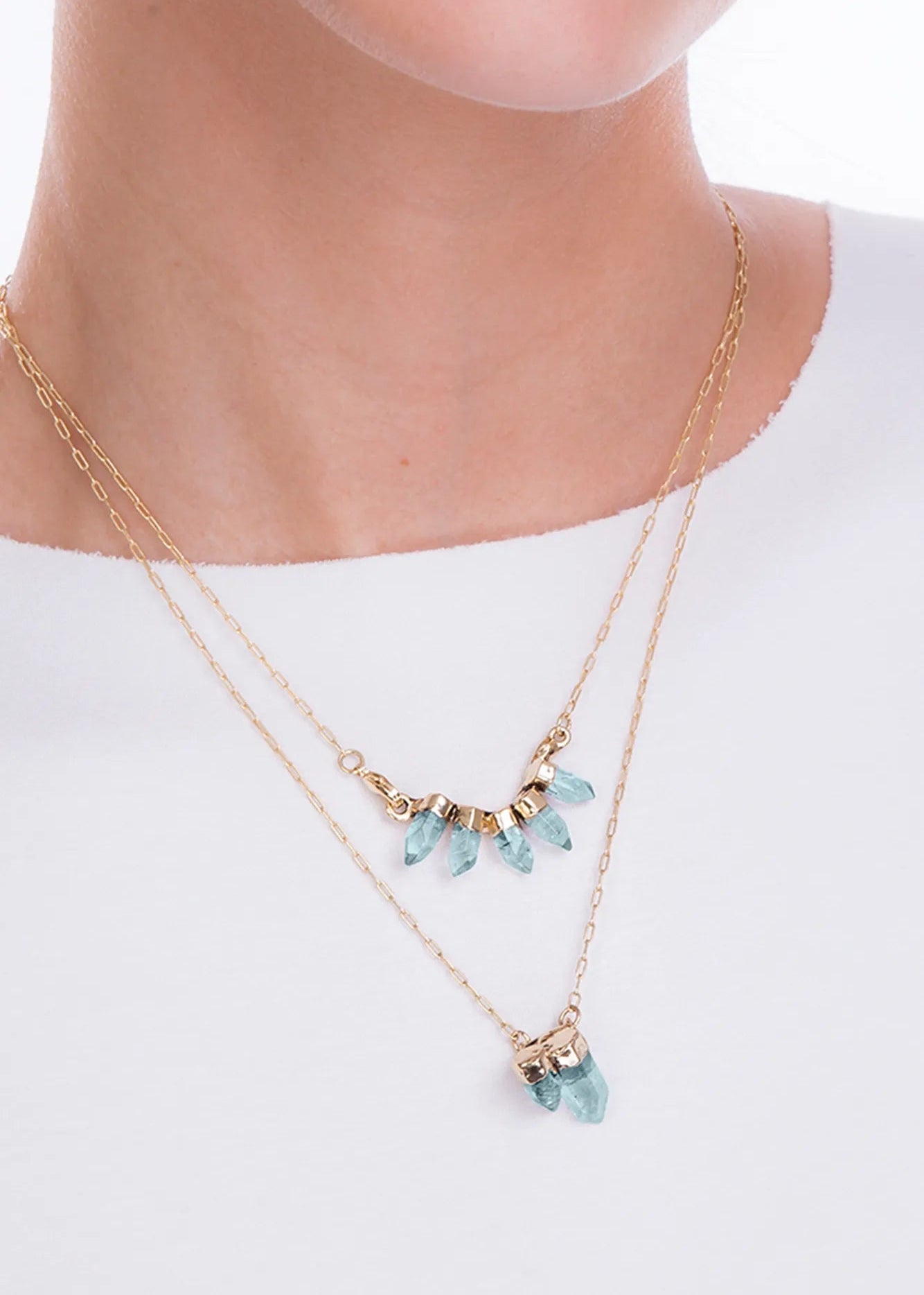 Gold necklace with turquoise beads worn by a person on a white background