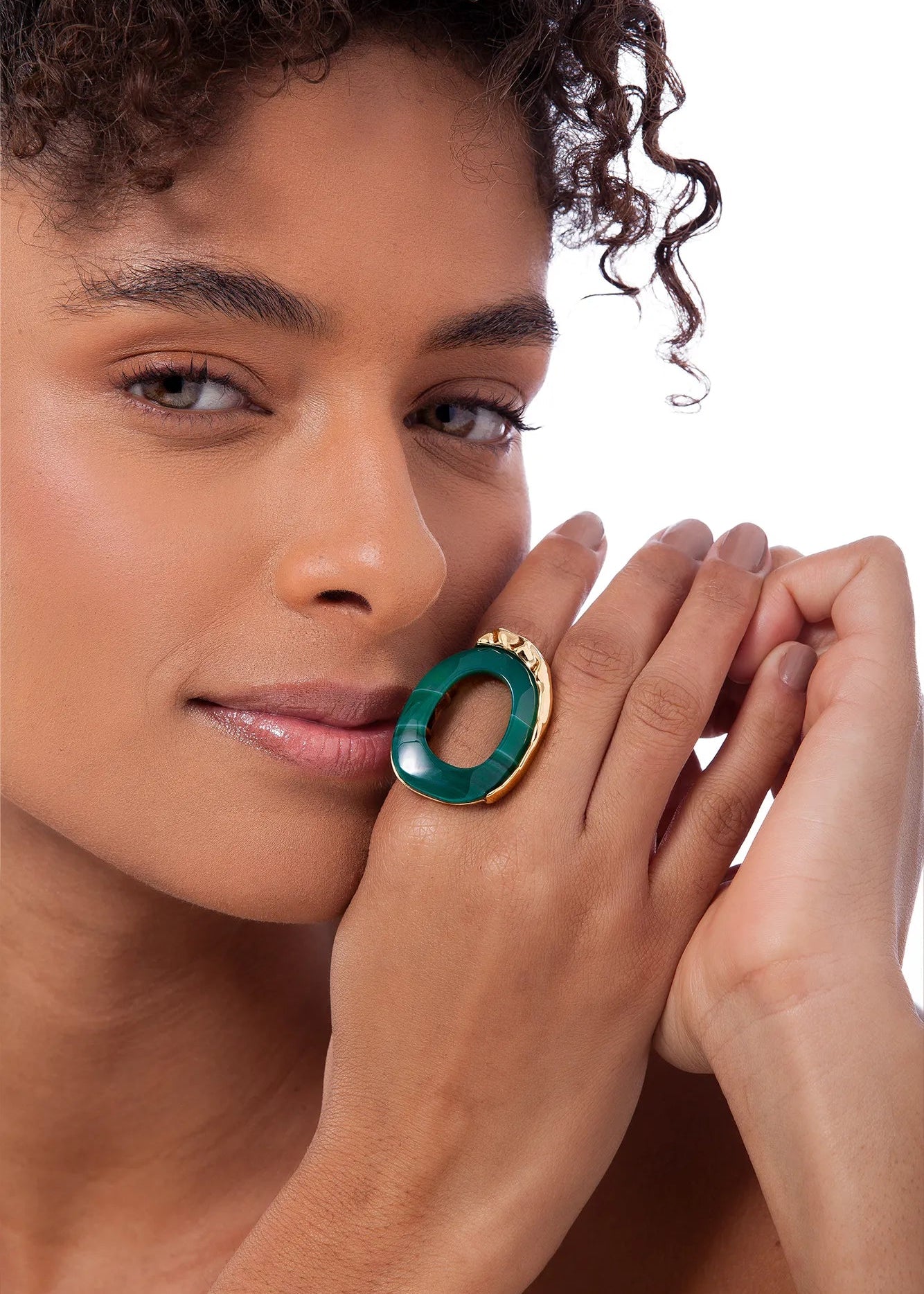 Woman wearing a green and gold ring on her finger against a white background