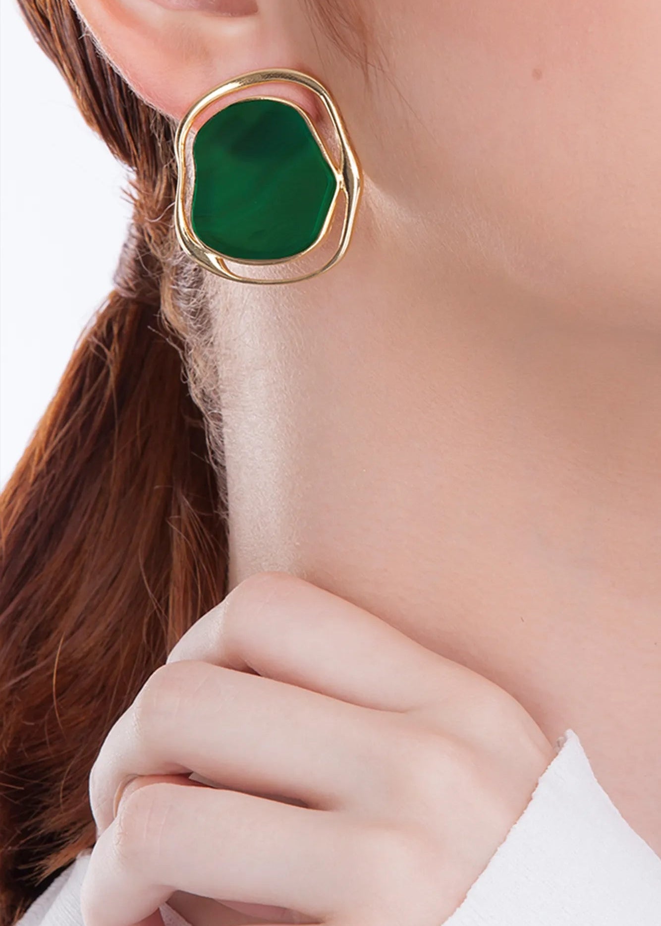 Green earring with gold frame on a person's ear
