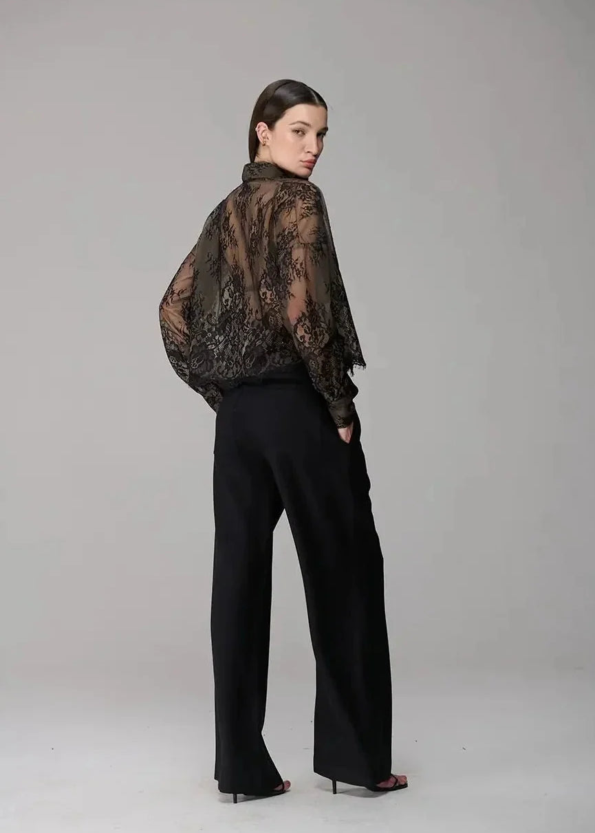 Woman wearing a sheer black lace top and black pants on a gray background