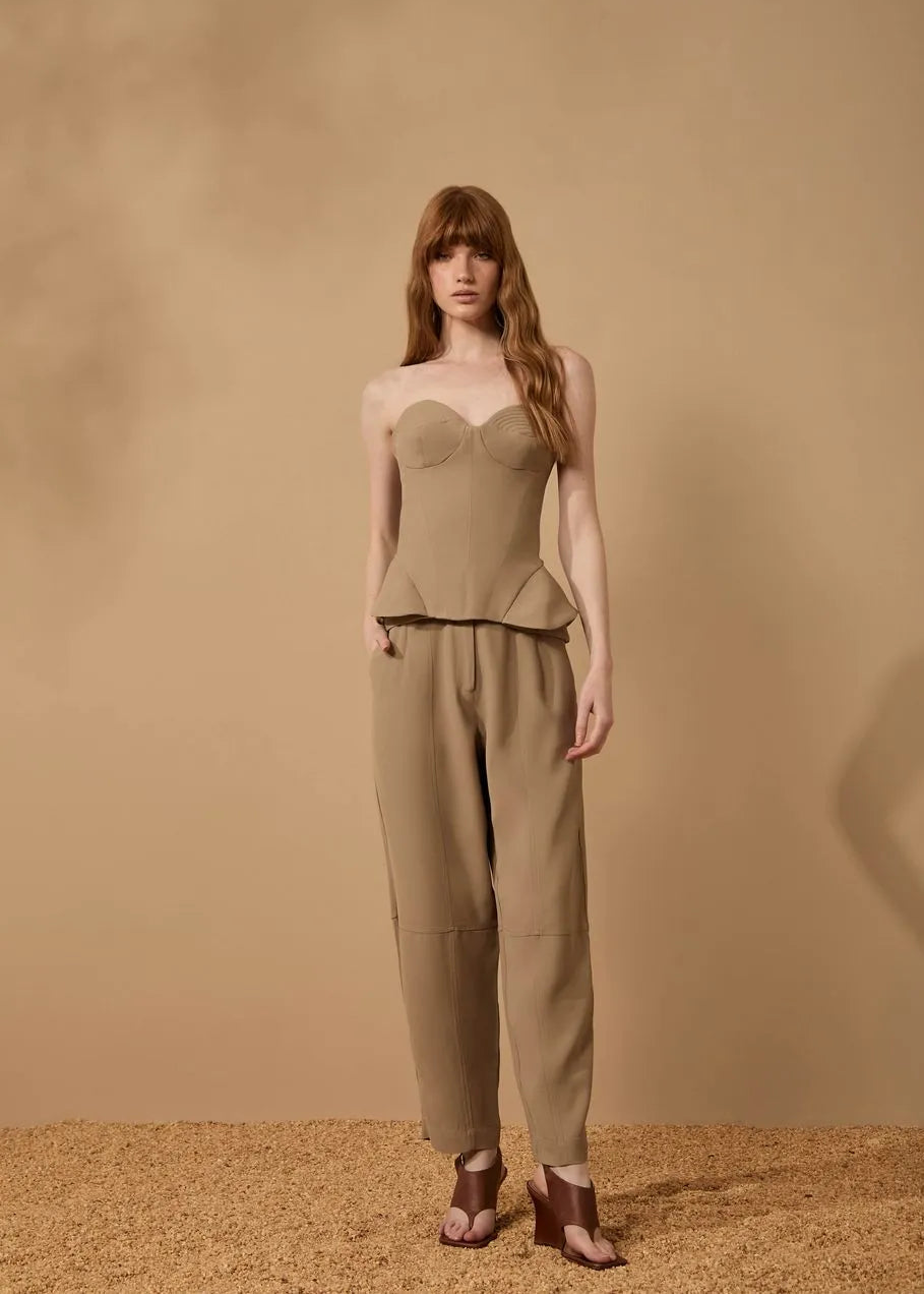 Woman wearing a beige strapless top and pants against a beige background