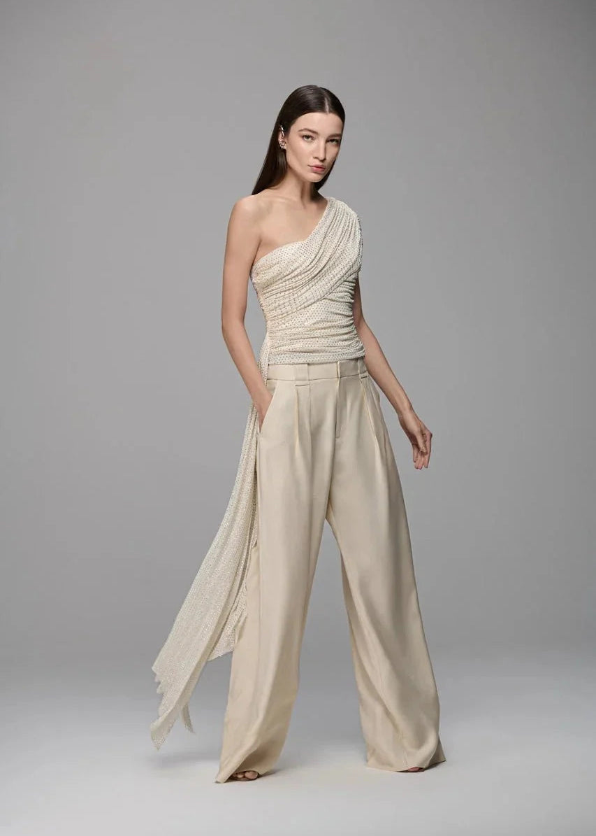 Woman wearing a beige one-shoulder jumpsuit on a gray background