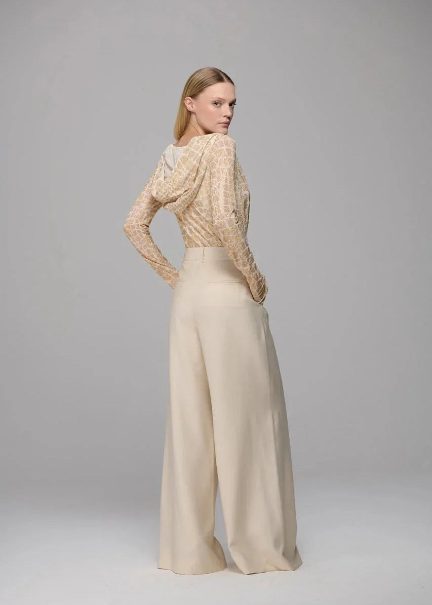 Woman wearing a beige knitted top and wide-leg pants on a gray background