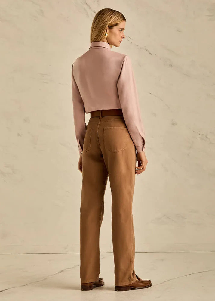 Woman wearing a pink blouse and brown pants against a beige background