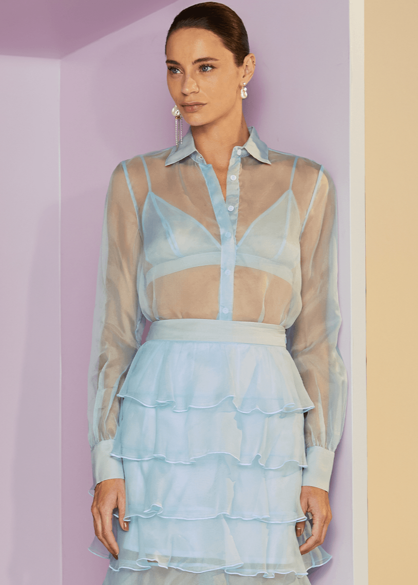 Woman wearing a light blue sheer dress against a pastel wall.