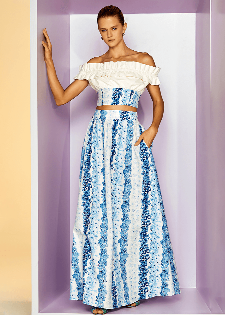 Woman wearing a white off-shoulder top and blue floral skirt against a purple background
