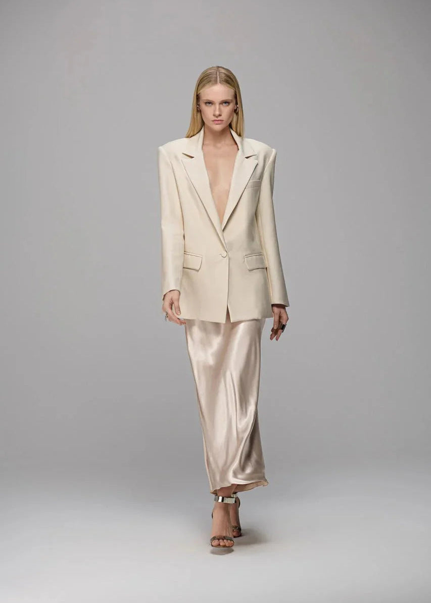 Woman wearing a beige suit with a high-low hem on a gray background