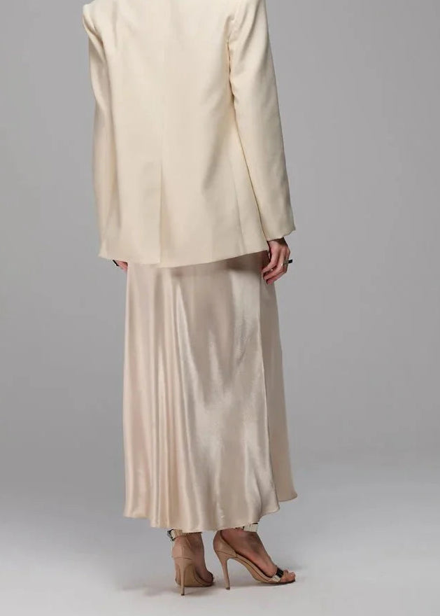 Woman wearing a beige suit standing against a gray background
