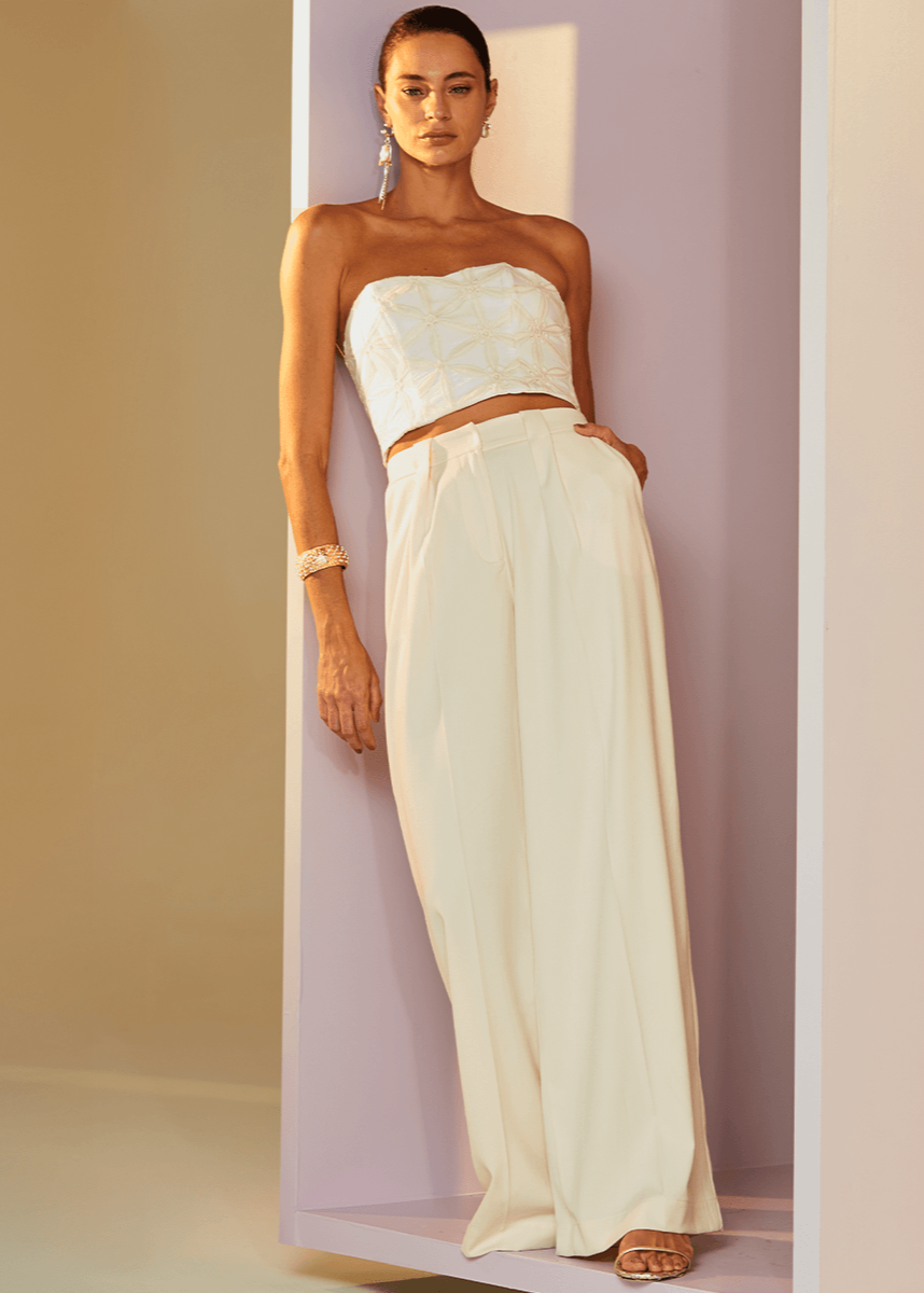 Woman wearing a strapless top and long white skirt against a plain background