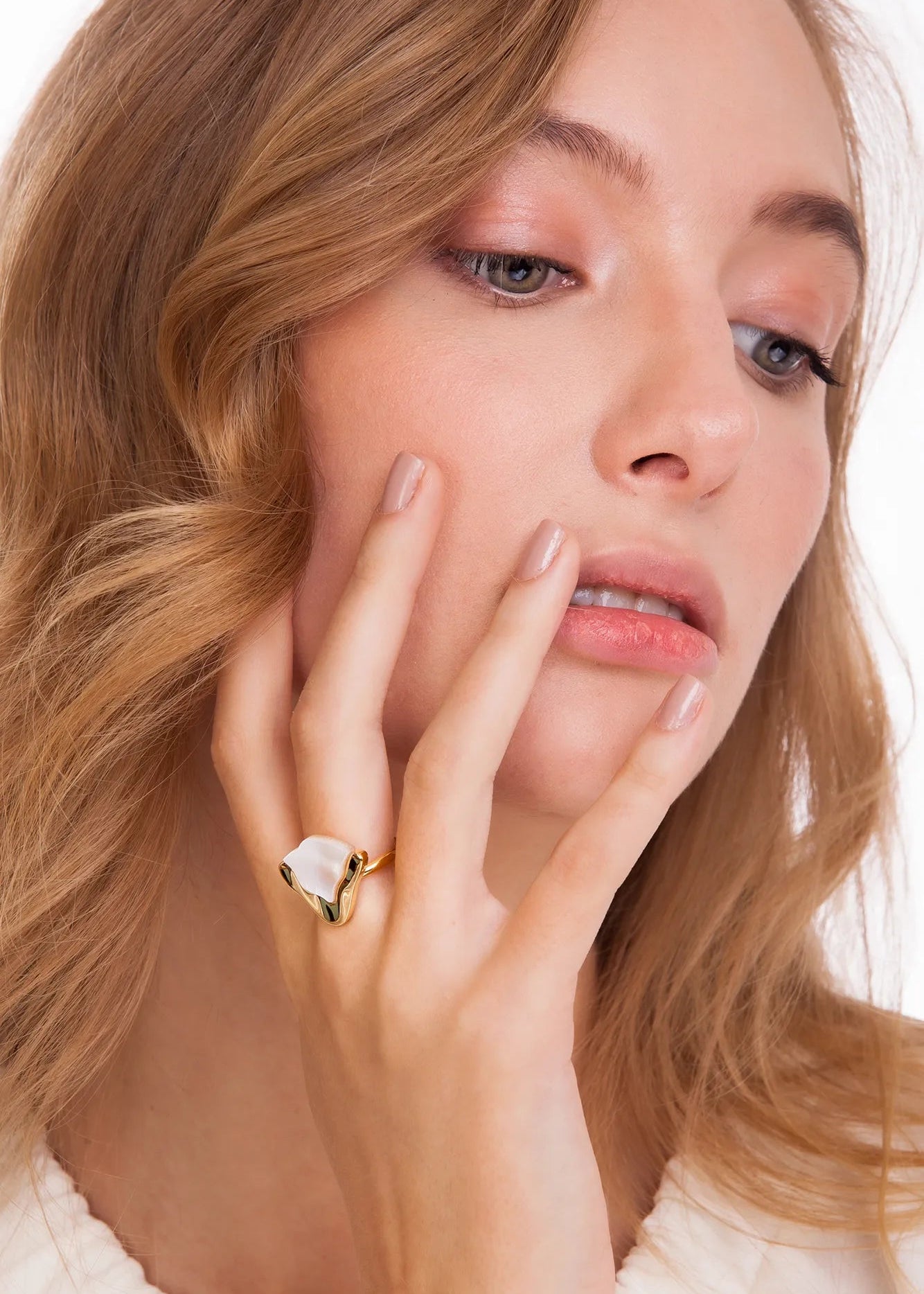 Woman wearing a gold ring with a clear stone, touching her face.