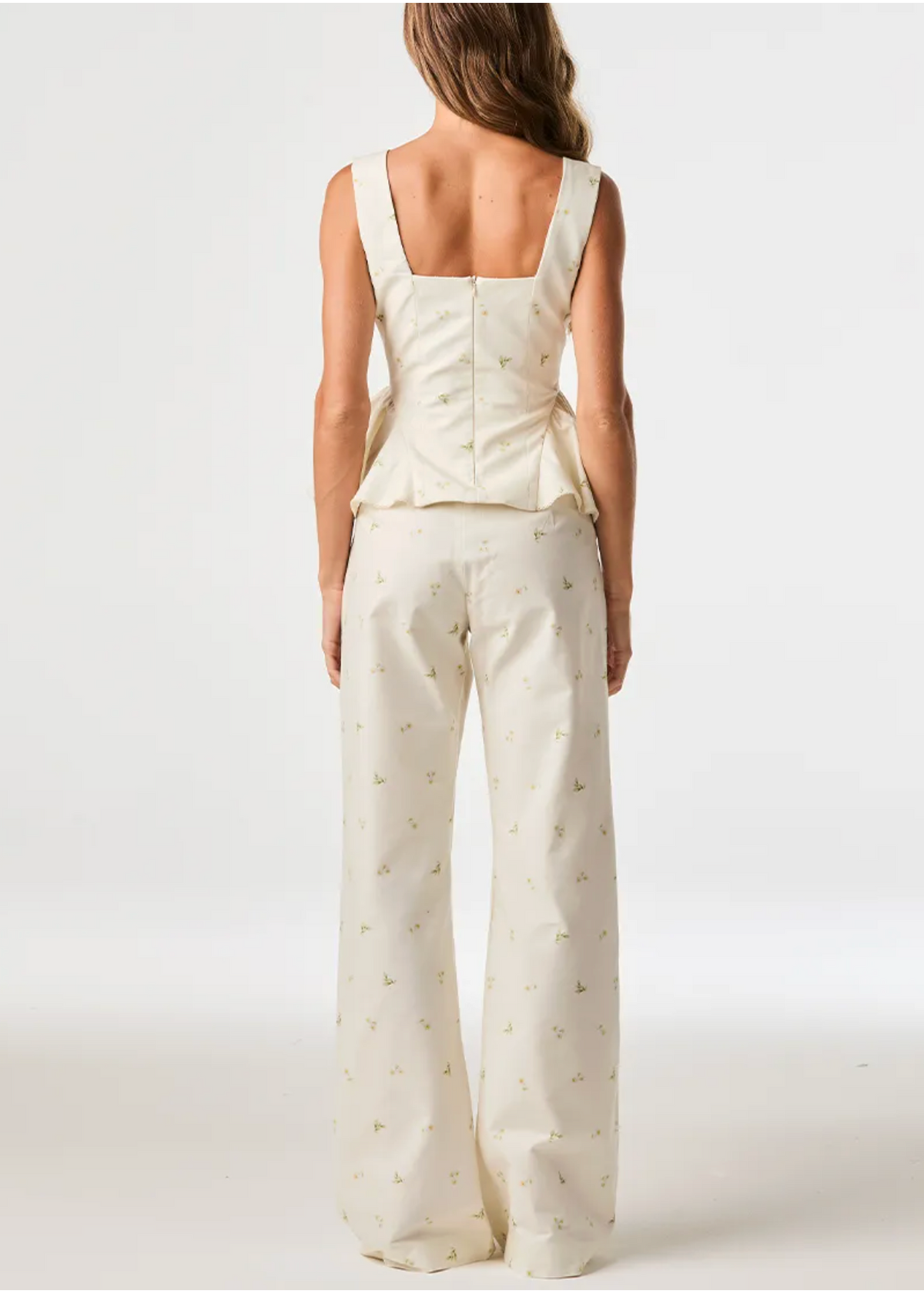 A woman shown from the back wearing a cream-colored sleeveless top and matching wide-leg pants with a small gold floral pattern, set against a plain white studio background.