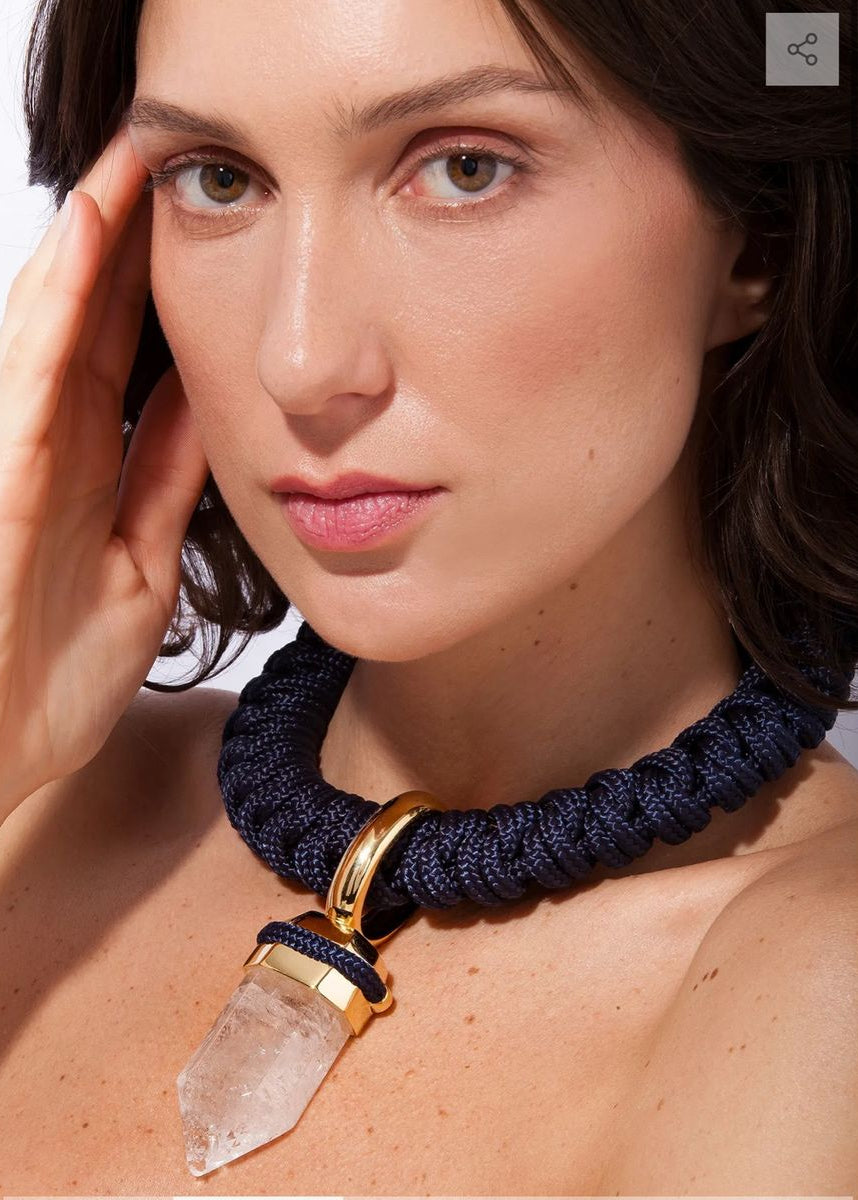 Woman wearing a dark blue necklace with a gold clasp and clear crystal pendant.