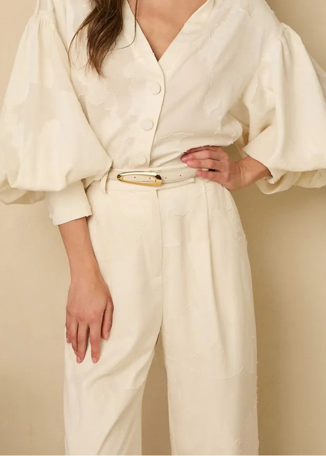 Woman wearing a white outfit with wide sleeves against a beige background