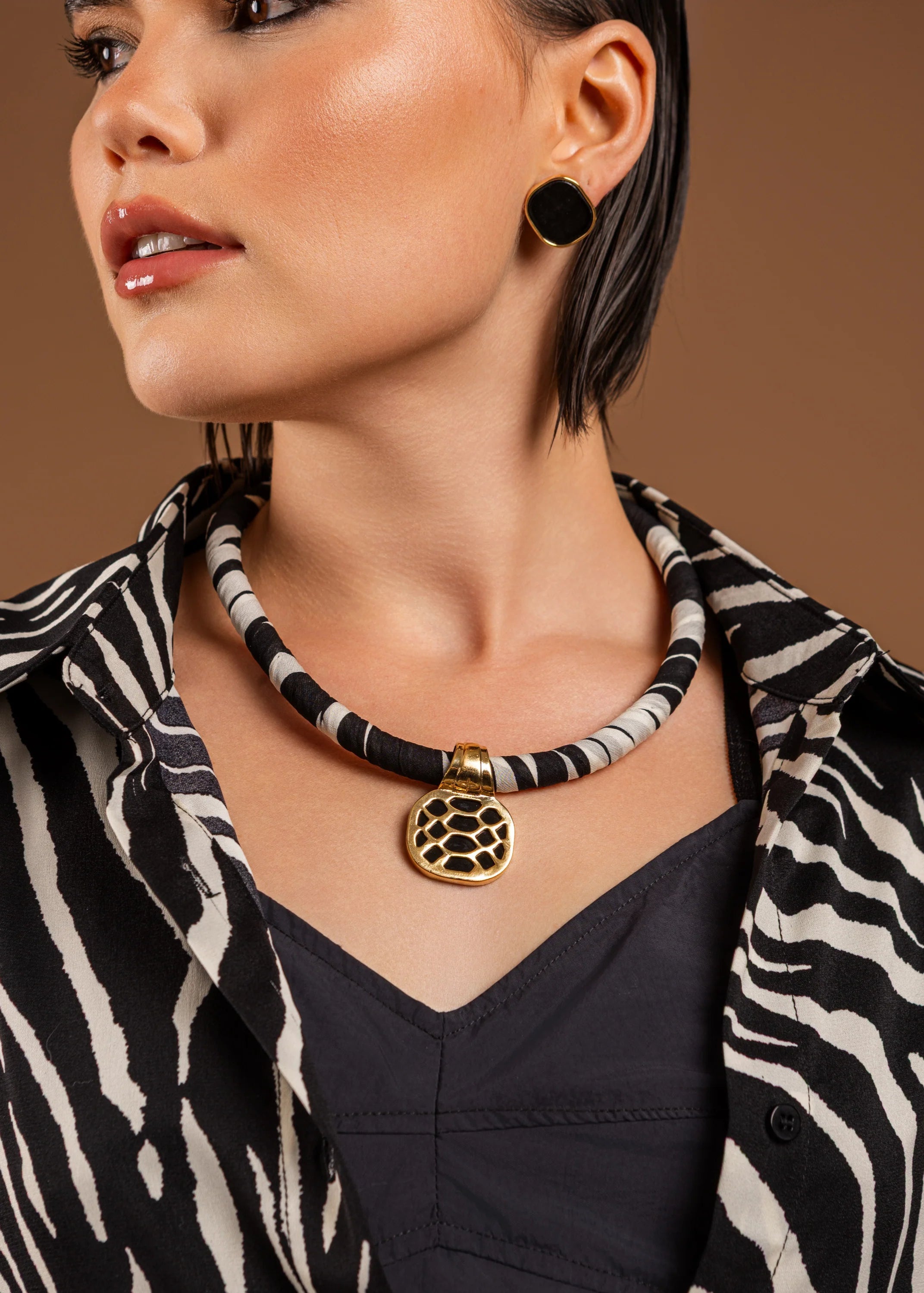 Woman wearing a black and white beaded necklace with a gold pendant on a brown background