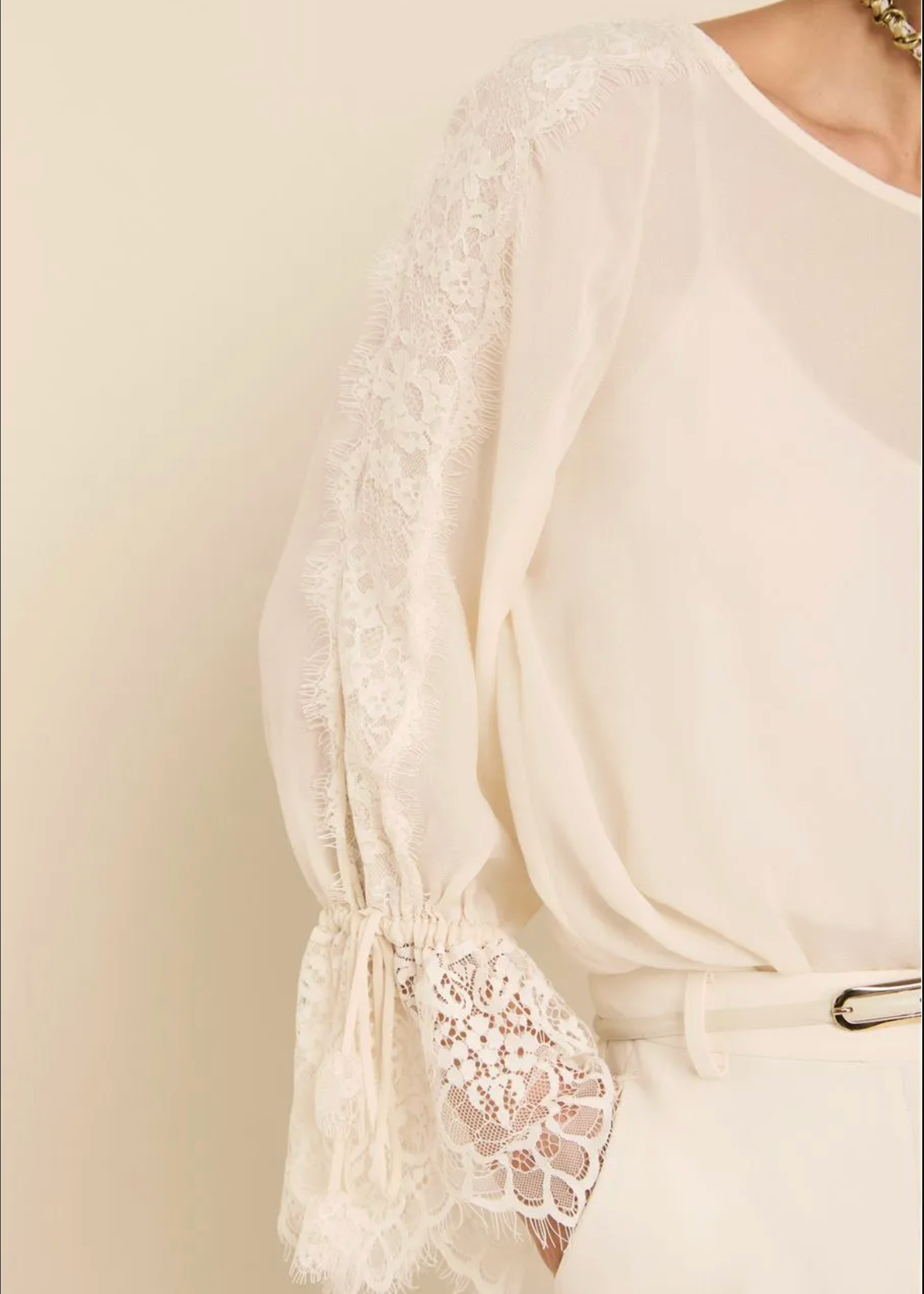 A close-up of a cream-colored blouse featuring sheer lace flutter sleeves with tie details at the cuffs, worn by a model.