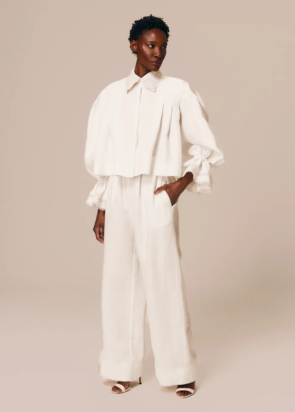 Woman wearing a white outfit with ruffled sleeves against a beige background