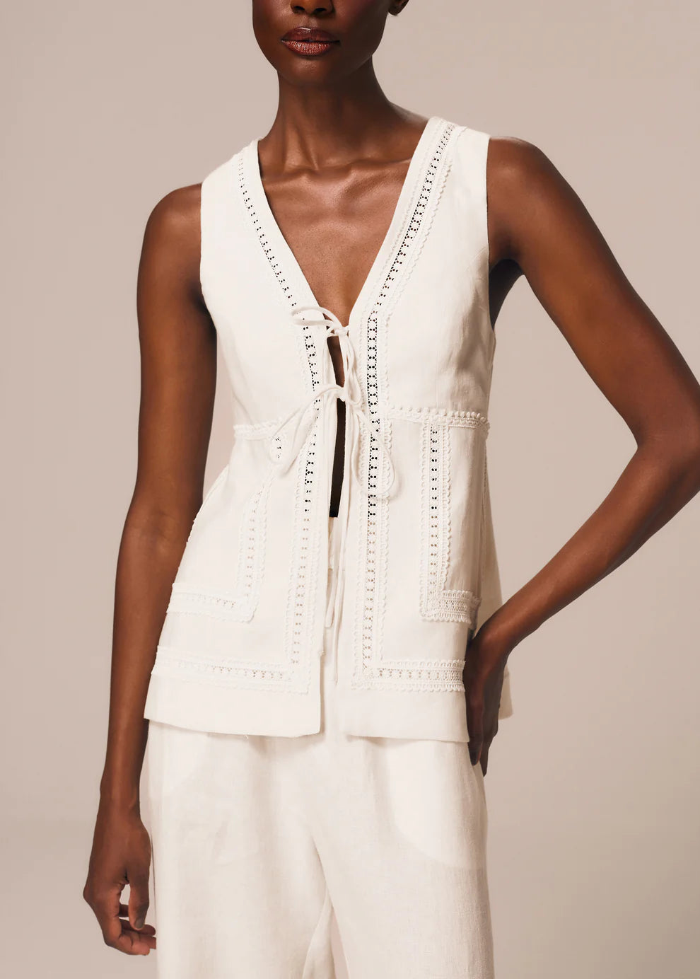 Woman wearing a white sleeveless top with lace details on a beige background