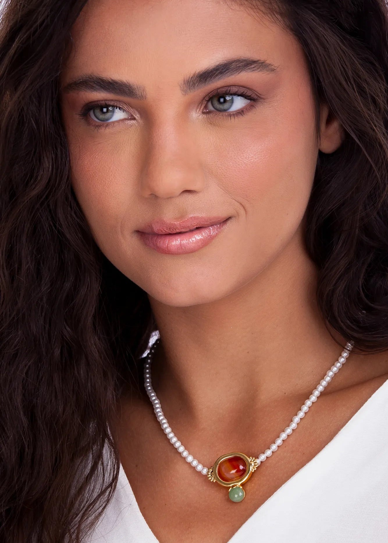 Woman wearing a pearl necklace with a colorful pendant against a neutral background