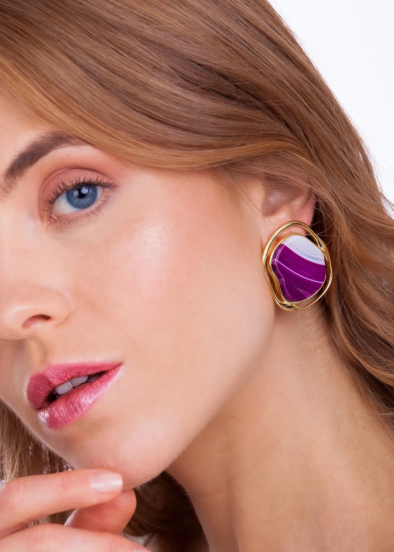 Close-up of a woman wearing a gold earring with a purple stone on a white background