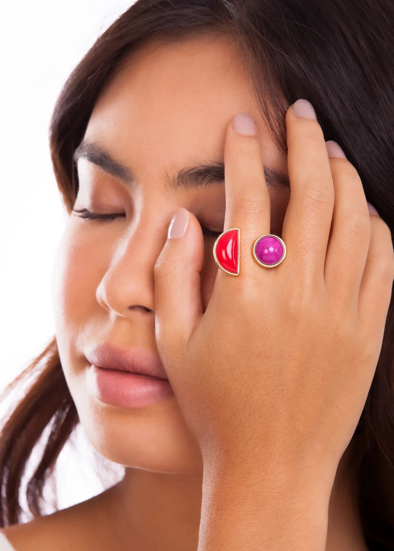 Close-up of a woman's face with a hand holding two colorful rings.
