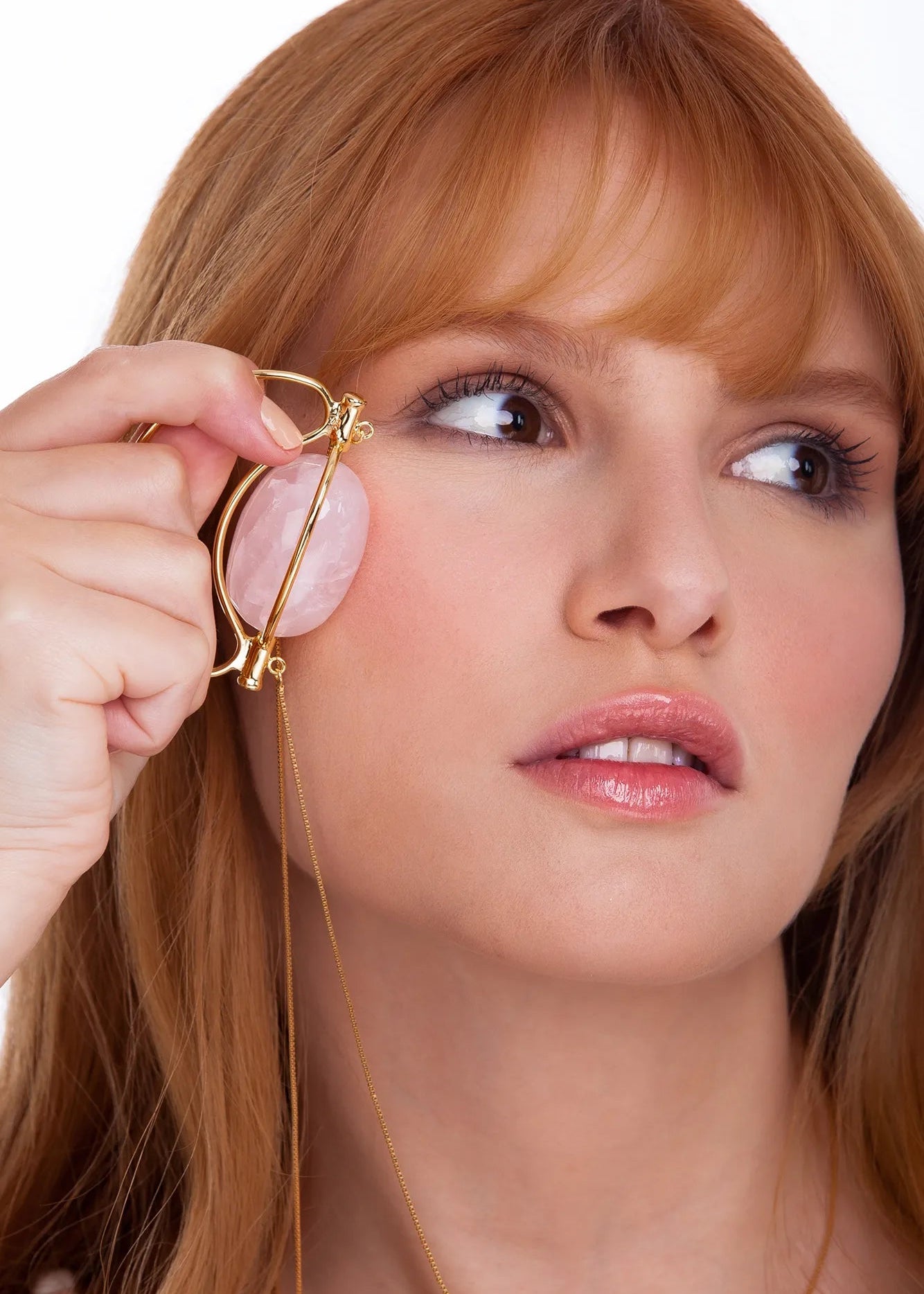 Woman using a gold makeup tool on her face against a white background