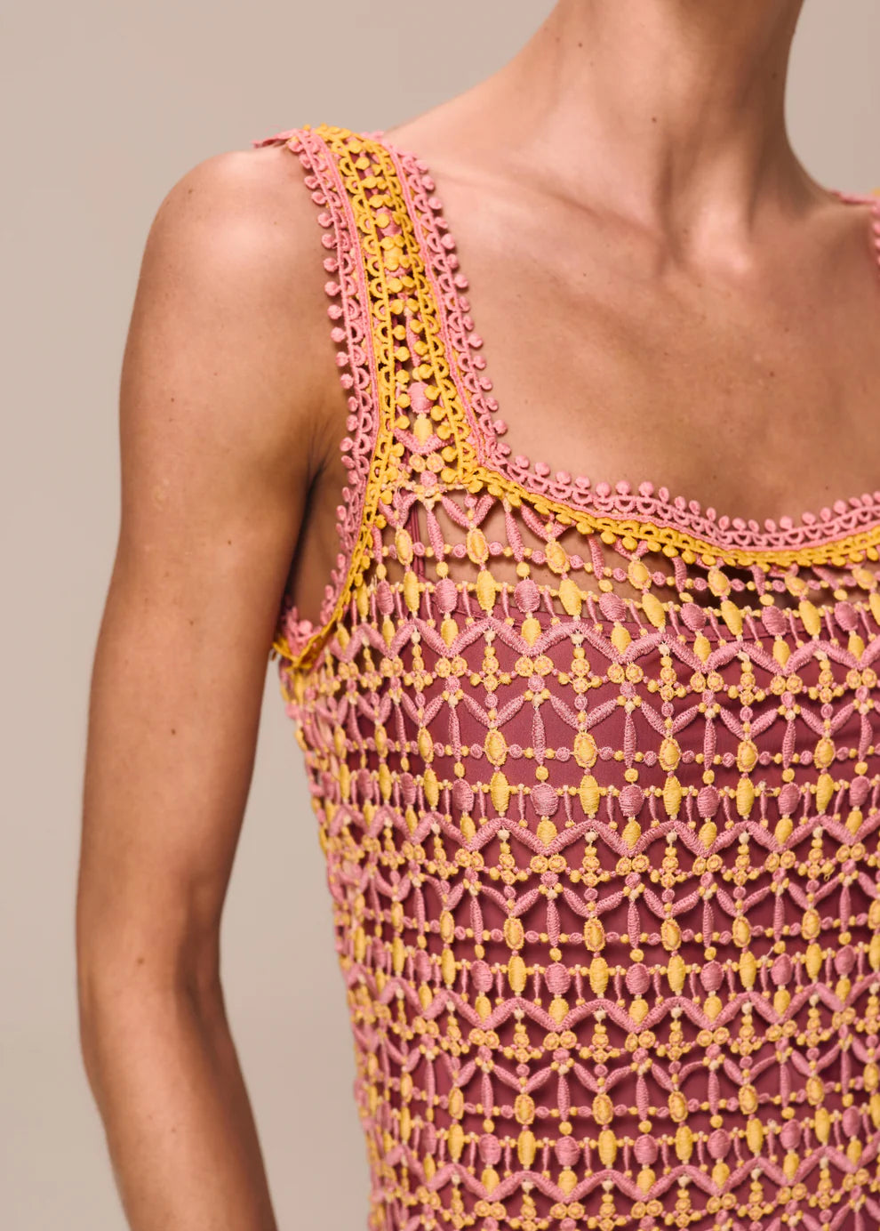 Close-up of a pink and yellow crochet dress on a neutral background