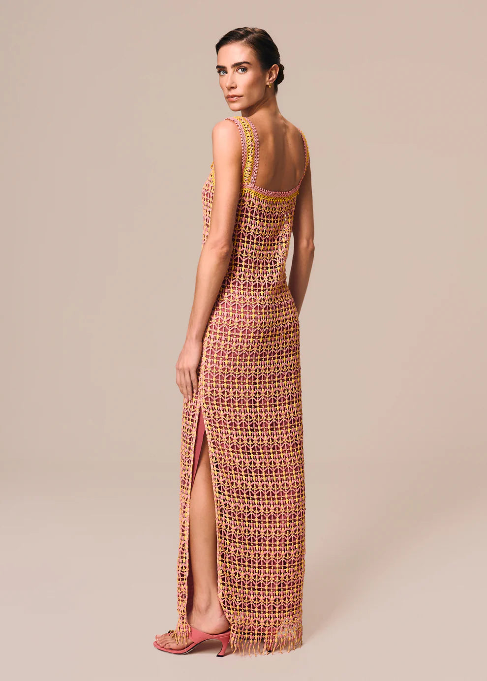 Woman wearing a long, patterned dress with a high slit on a beige background