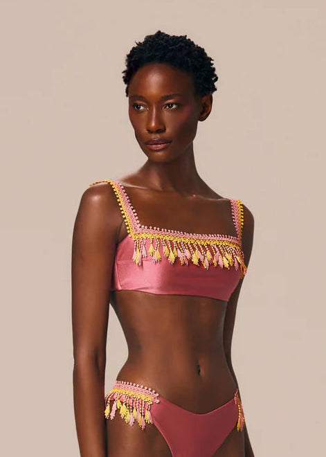 Woman wearing a pink bikini with gold fringe details on a beige background