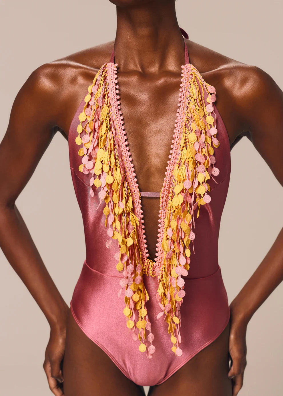 Pink swimsuit with yellow fringe details on a neutral background