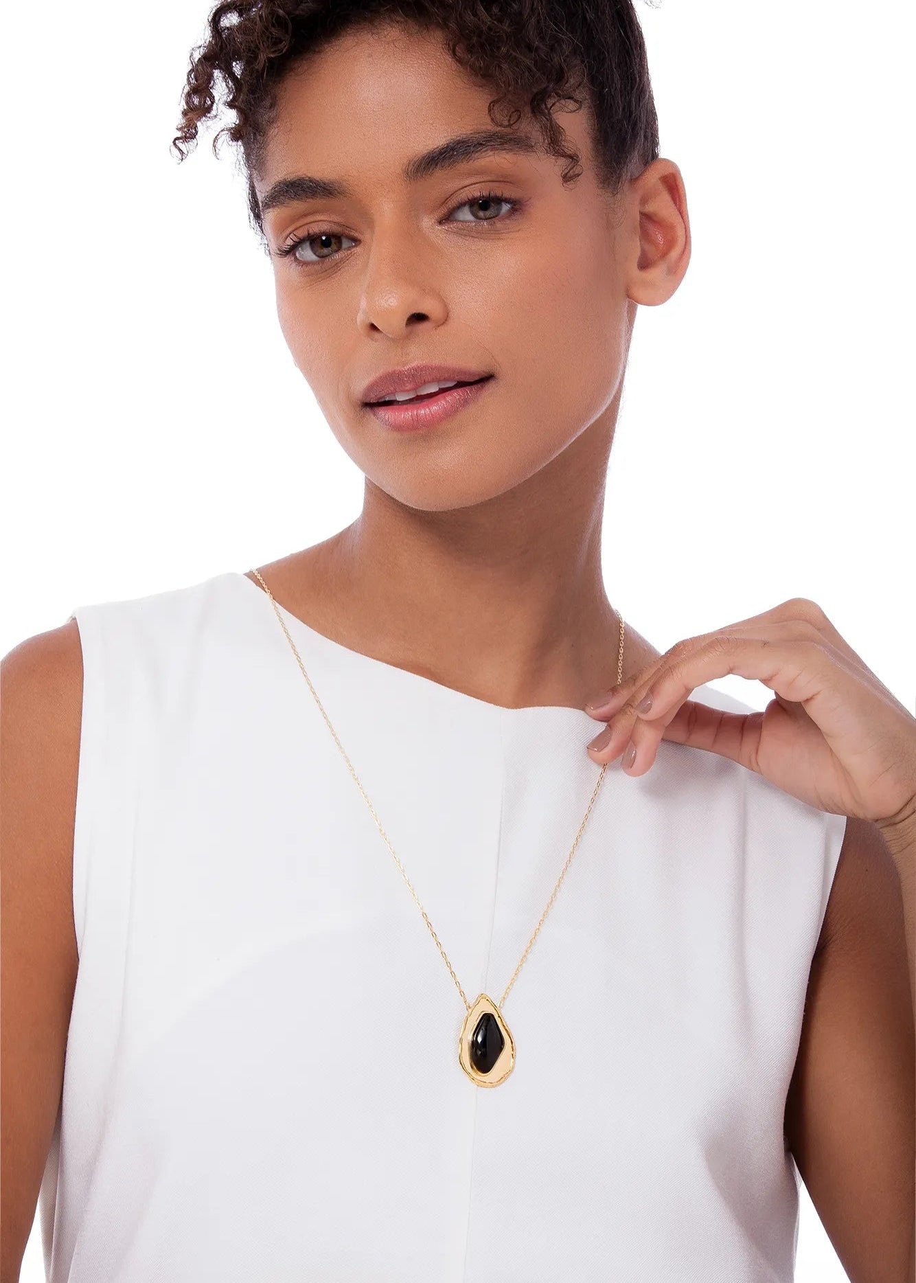Woman wearing a gold necklace with a black pendant on a white background