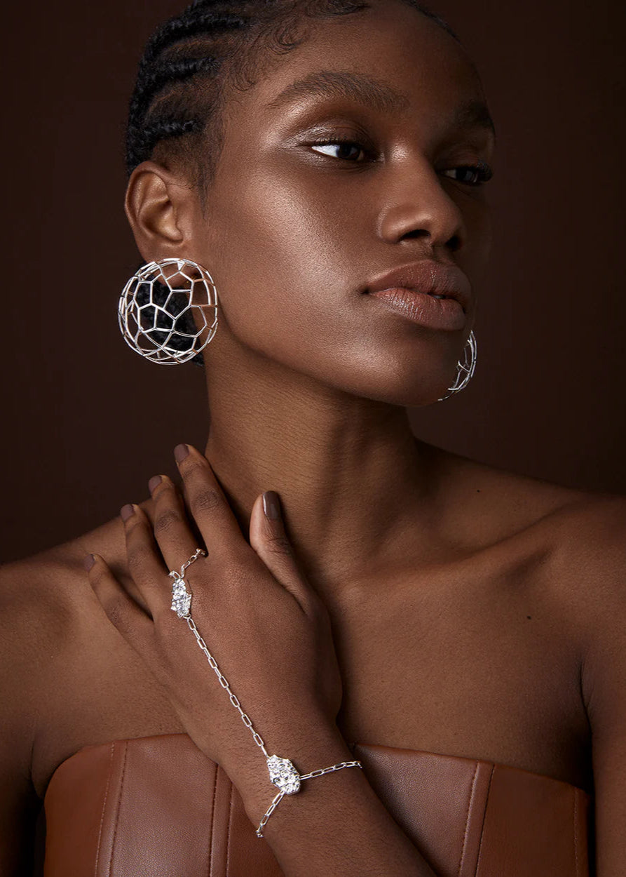 Woman wearing silver hoop earrings and bracelet against a brown background