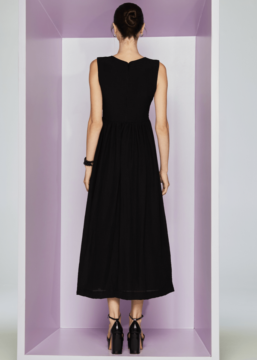 Woman wearing a black sleeveless dress standing in a minimalistic setting with a purple box.