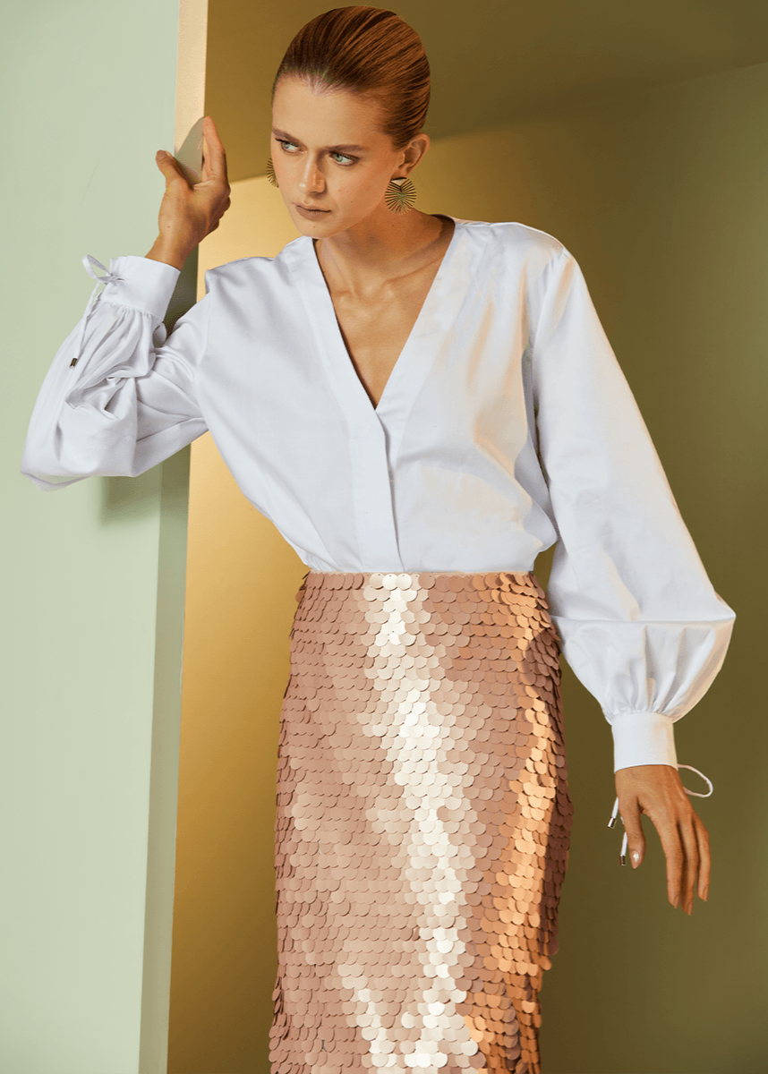 Woman wearing a white blouse and pink sequin skirt against a neutral background