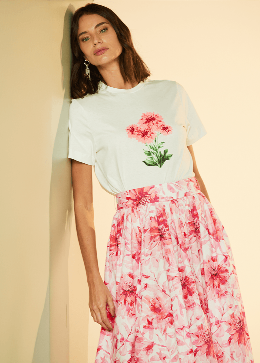 Woman wearing a white t-shirt with a floral design and a pink floral skirt against a beige background