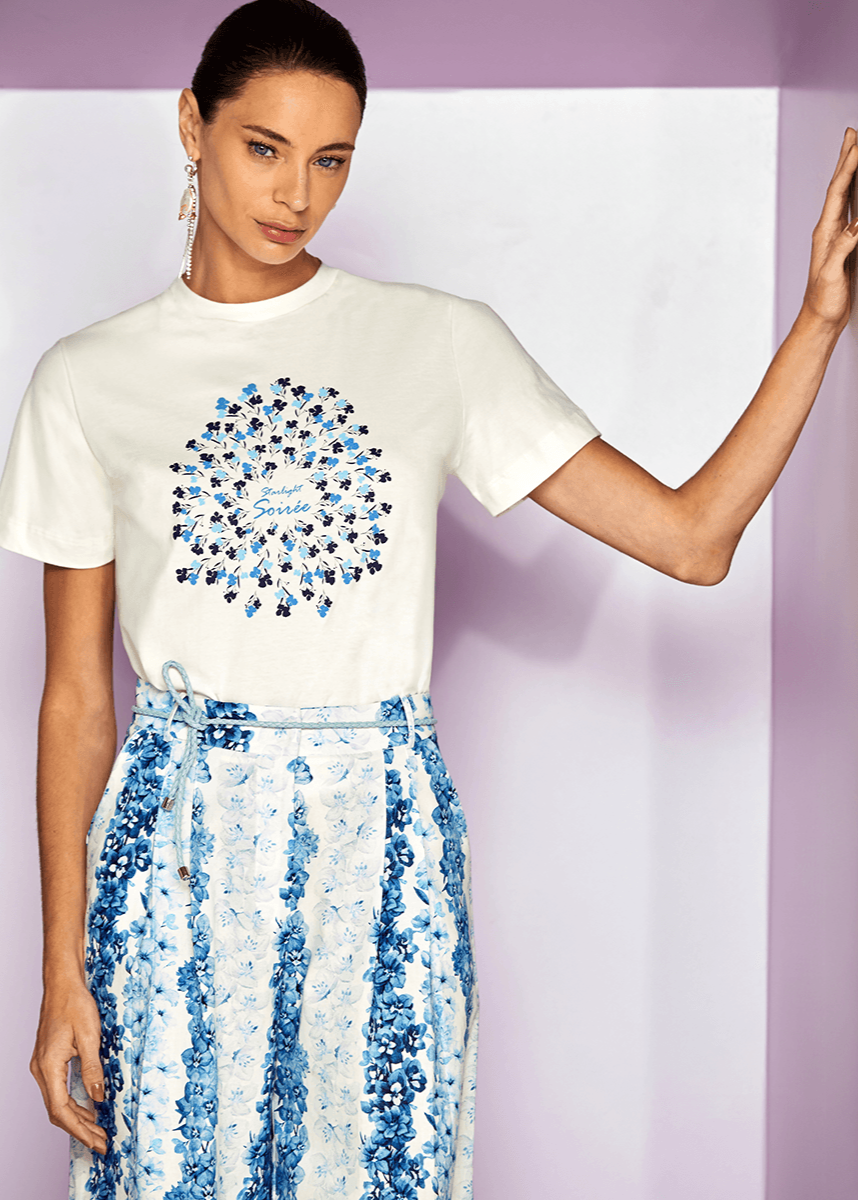 Woman wearing a white t-shirt with a blue floral design and a matching skirt against a light purple background