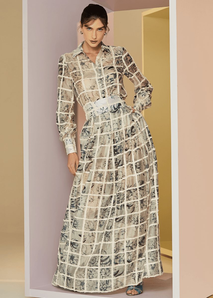 Woman wearing a long, patterned dress standing in a minimalistic room with neutral colors.
