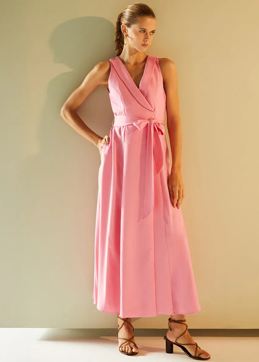 Woman wearing a pink dress standing against a plain wall.