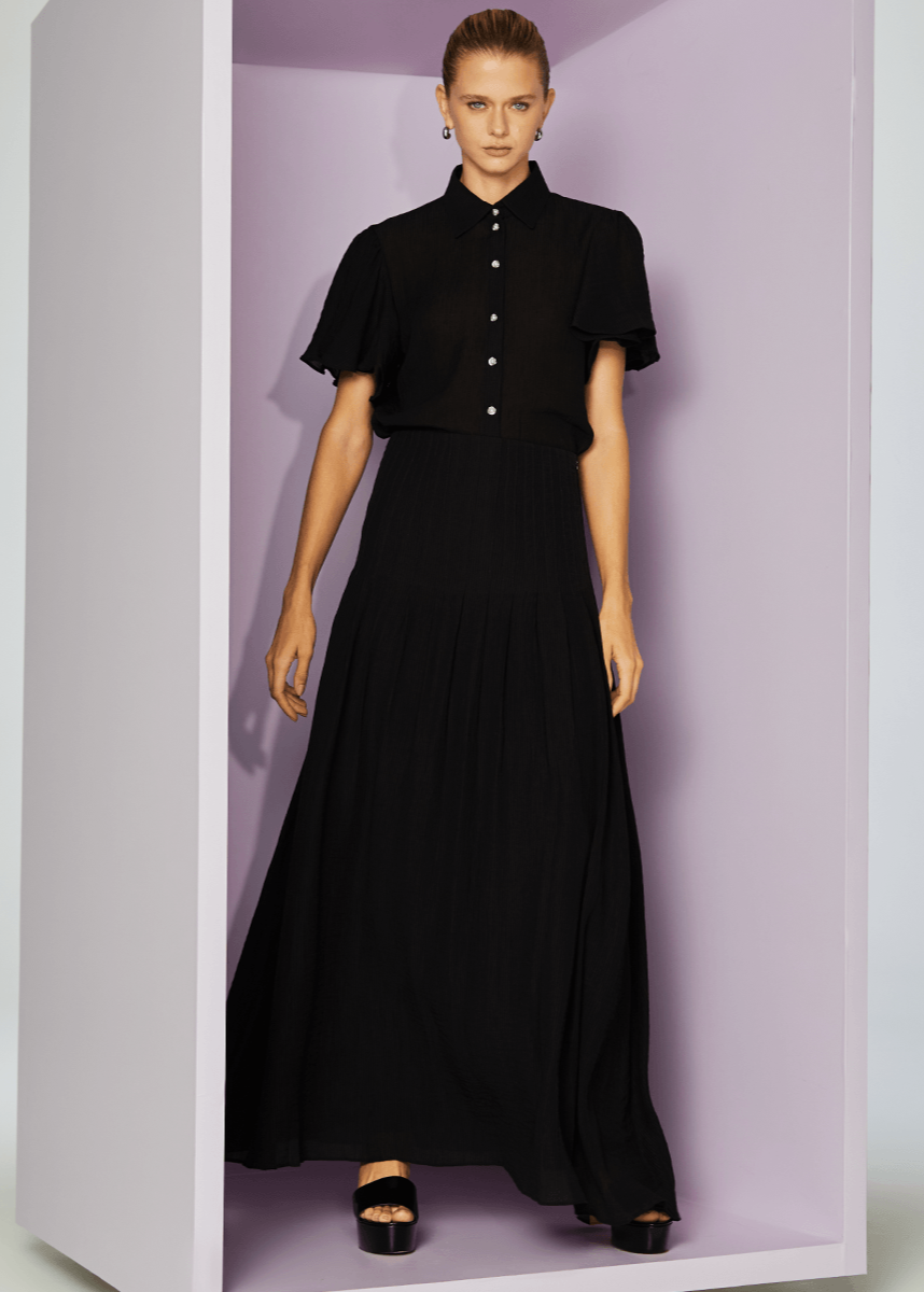 Woman wearing a black dress with a high collar and long skirt in a minimalistic setting.