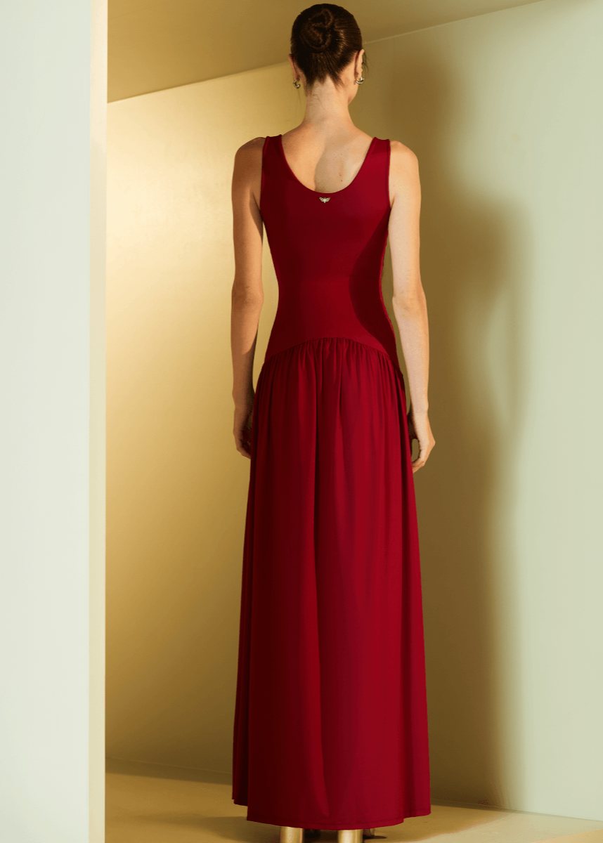 Woman wearing a long red dress against a plain wall.