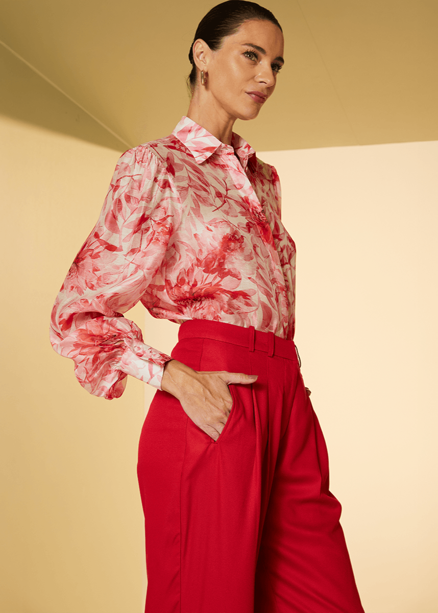 Woman wearing a red and white patterned blouse and red pants on a beige background