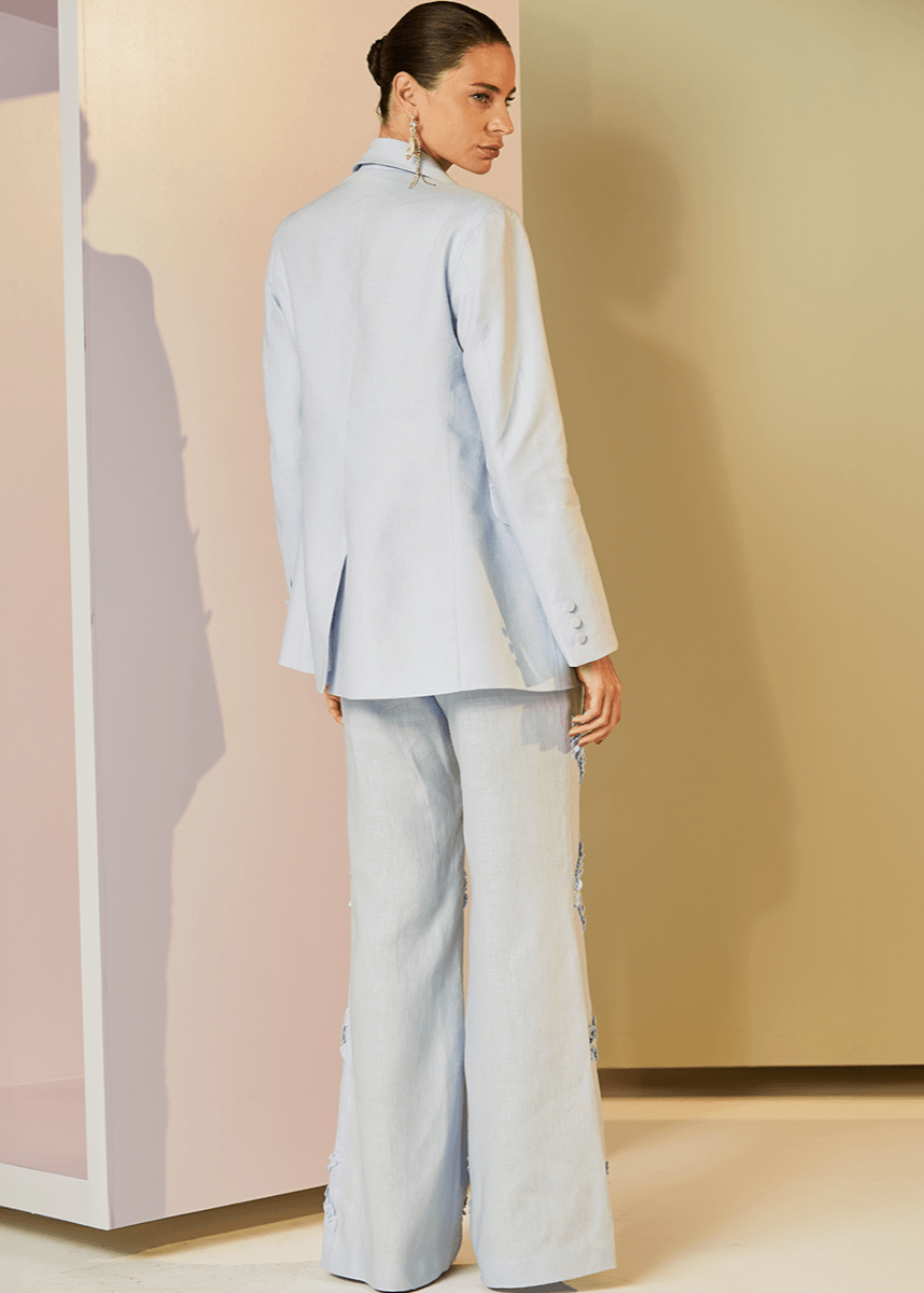 Woman in a light blue suit standing in front of a mirror with a minimal background
