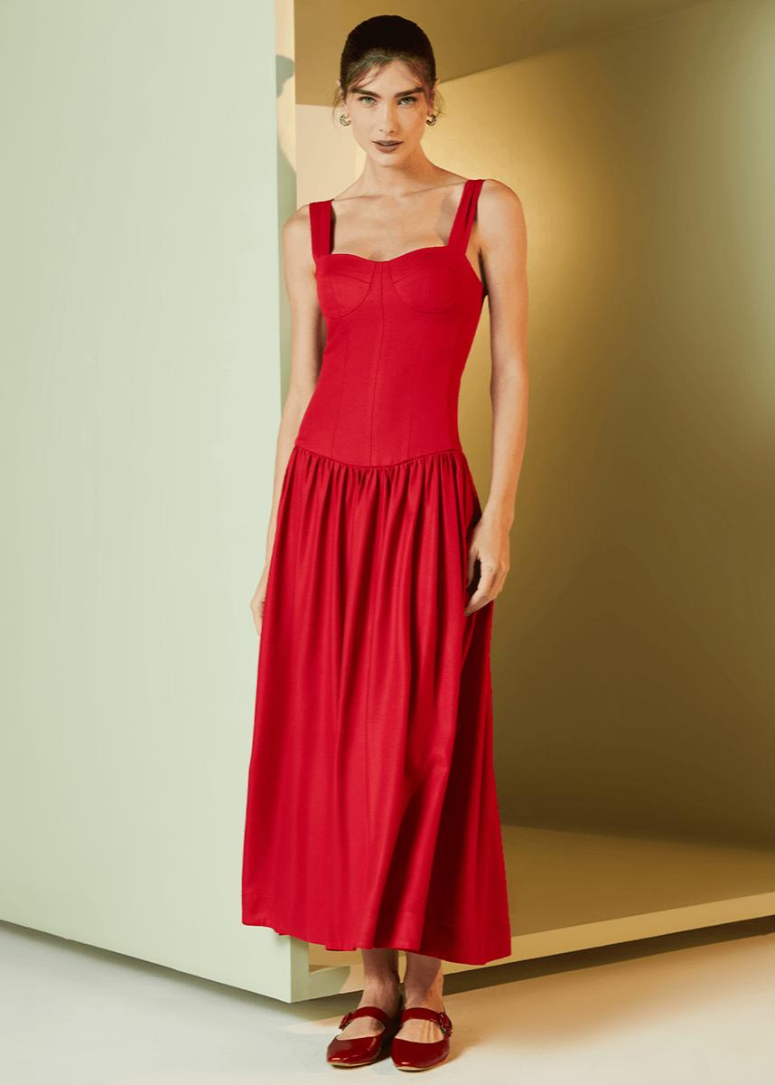 Woman wearing a red dress standing against a neutral wall.